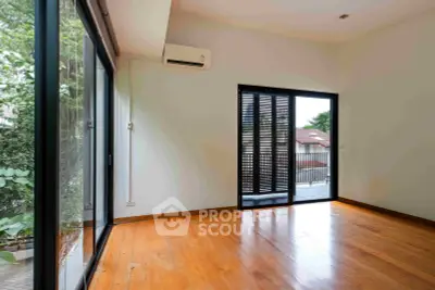 Spacious empty room with wooden flooring and large windows opening to a balcony with a view.