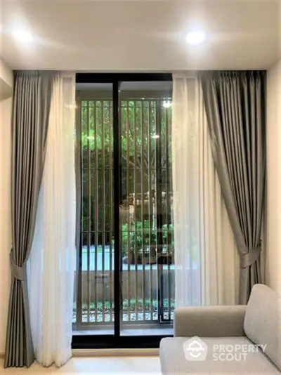 Serene living room with elegant gray drapery framing a large window overlooking lush greenery, complemented by a cozy modern sofa.