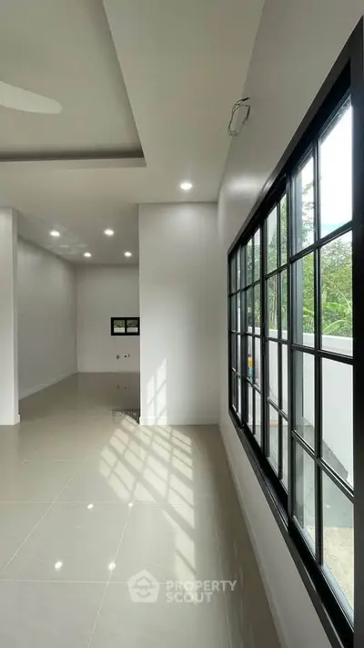 Spacious modern living room with large windows and glossy tiled floors, offering abundant natural light.