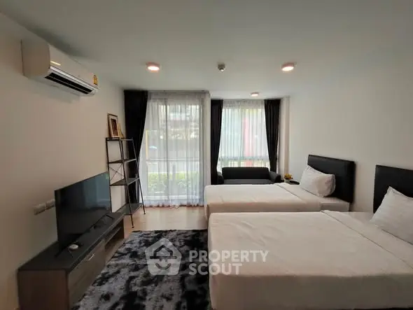 Modern bedroom with twin beds, stylish decor, and natural light from large windows.