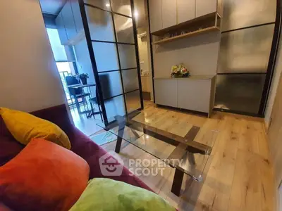 Modern living room with glass coffee table and colorful cushions, featuring sleek wooden flooring and stylish decor.