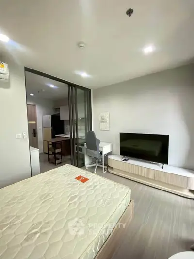 Modern studio apartment with sleek design, featuring a cozy bed, TV, and compact kitchen area.