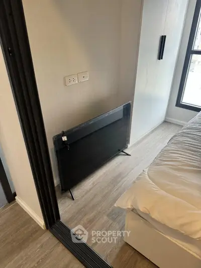 Modern bedroom with sleek flooring and large window, featuring a mounted TV for a cozy living experience.