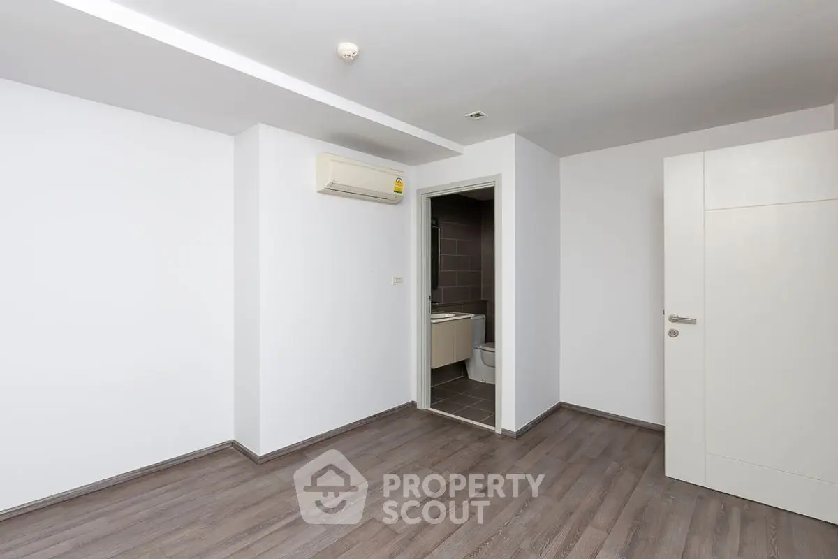 Spacious empty room with wooden flooring and bathroom access