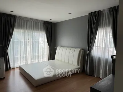 Spacious bedroom with large windows and elegant curtains, featuring a modern bed frame.
