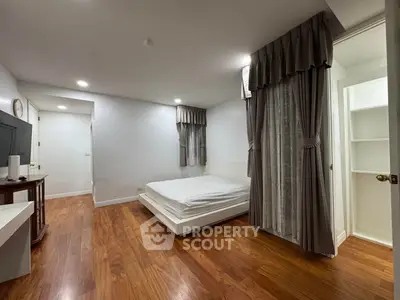 Spacious bedroom with wooden flooring and elegant curtains in modern apartment.