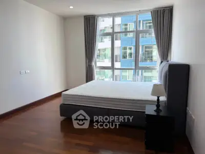 Spacious bedroom with large window and modern furnishings in a high-rise apartment.