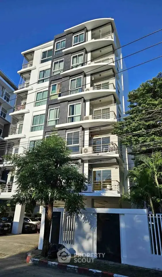 Modern multi-story residential building with balconies and lush greenery.