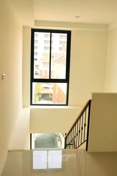 Bright stairwell with large window and modern railing in residential building.