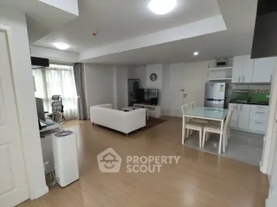 Spacious open-plan living room with modern kitchen and dining area, featuring sleek furniture and natural light.