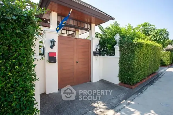 Elegant entrance of a modern home with lush greenery and secure wooden gate.