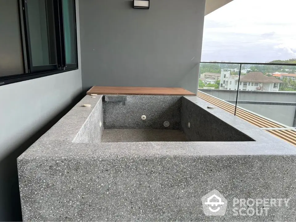 Modern balcony with concrete bathtub and glass railing offering scenic views.