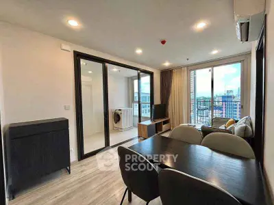 Modern living room with dining area and city view, featuring sleek furniture and large windows.