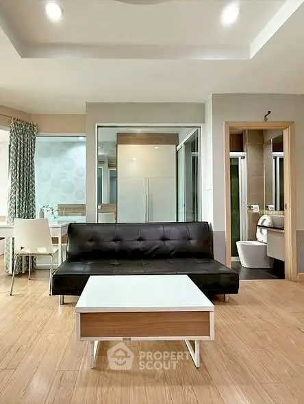 Modern living room with sleek black sofa, stylish coffee table, and open layout leading to dining area.