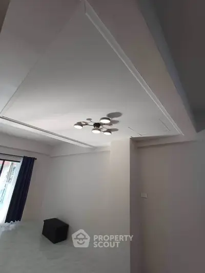 Modern minimalist bedroom with unique ceiling light fixture and natural light from window.