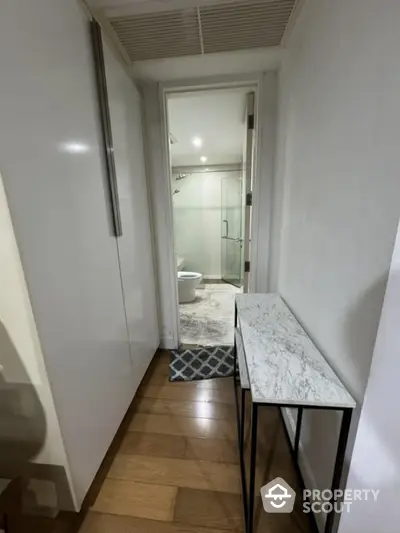 Modern hallway leading to a sleek bathroom with glass shower enclosure.