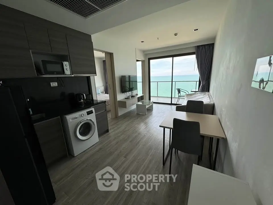 Modern open-plan living room with ocean view, featuring sleek kitchen and dining area.