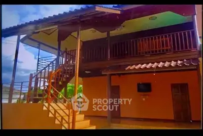 Charming two-story home with wooden balcony and exterior staircase, perfect for tropical living.
