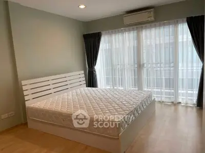 Spacious bedroom with large windows and natural light, featuring a comfortable bed and modern decor.