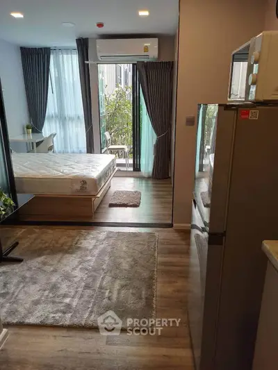 Modern studio apartment with cozy bedroom and compact kitchen area, featuring large windows and stylish decor.