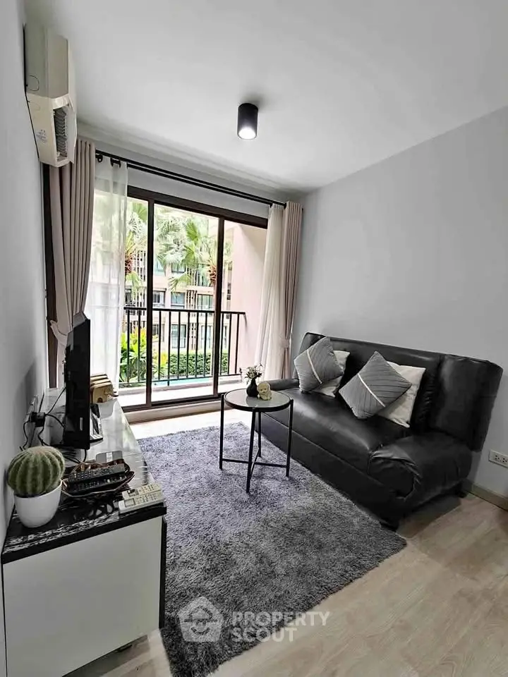 Modern living room with sleek black sofa and large window overlooking lush greenery.