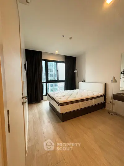 Spacious bedroom with large window and modern furnishings in a high-rise apartment.