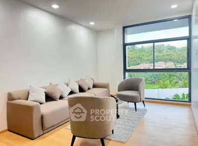 Modern living room with large window and stylish furniture overlooking lush greenery.