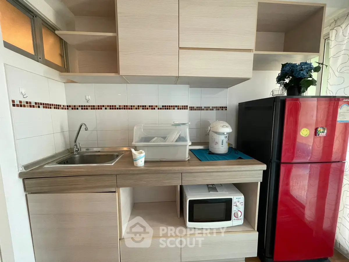 Modern kitchen with red fridge, microwave, and sleek cabinetry in a compact layout.
