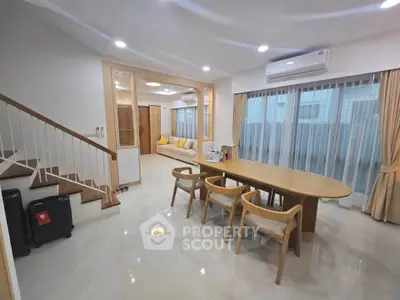Spacious modern living room with dining area and staircase, featuring elegant furniture and natural lighting.