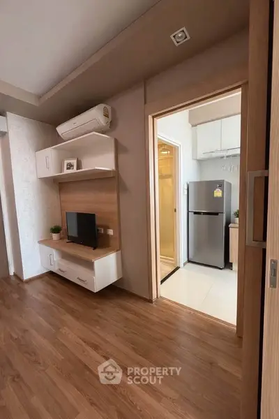 Modern apartment interior with wooden flooring, compact living area, and kitchen featuring stainless steel fridge.