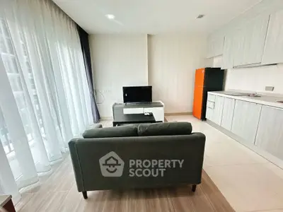 Modern living room with sleek kitchen and vibrant orange fridge in open layout apartment.