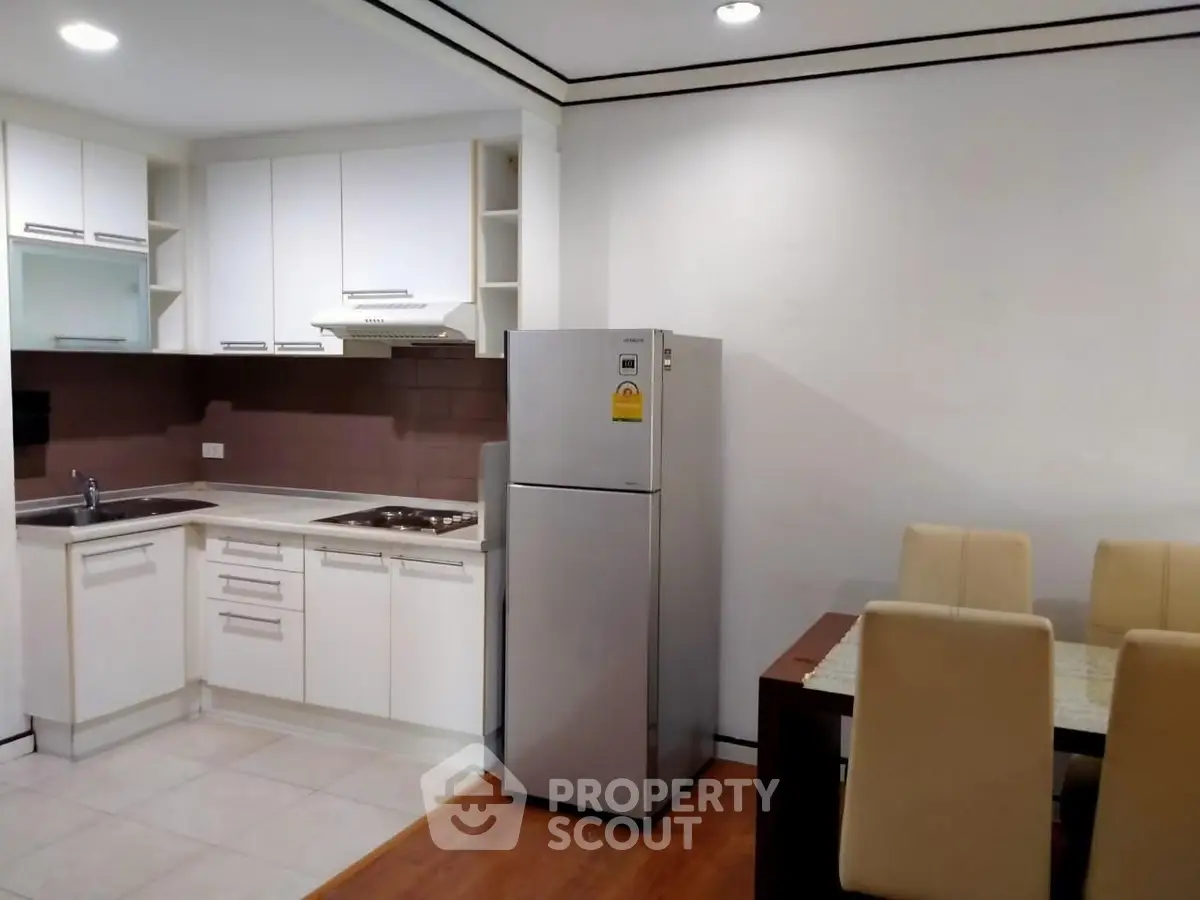 Modern kitchen with dining area, featuring sleek cabinets and stainless steel fridge.