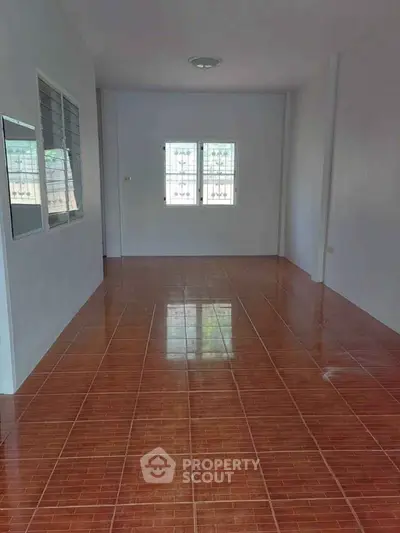 Spacious empty room with tiled flooring and natural light from windows.