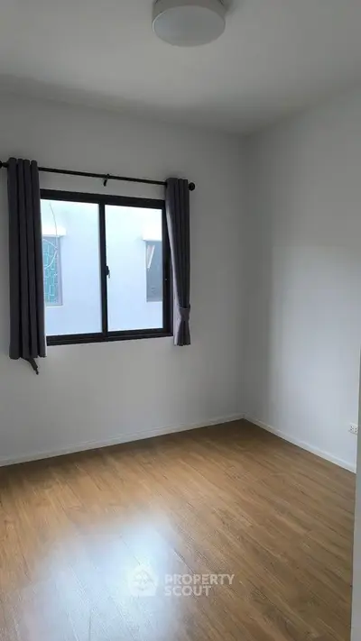 Spacious empty room with wooden flooring and large window, perfect for customization.