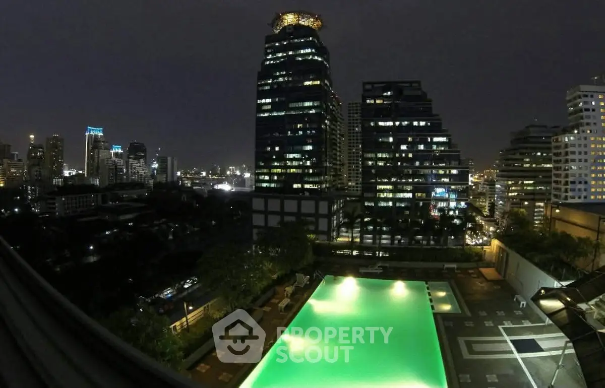 Stunning night view of illuminated rooftop pool with city skyline backdrop, perfect for luxury urban living.