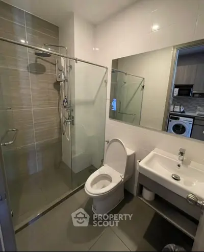Modern bathroom with glass shower, toilet, and sink in sleek apartment.