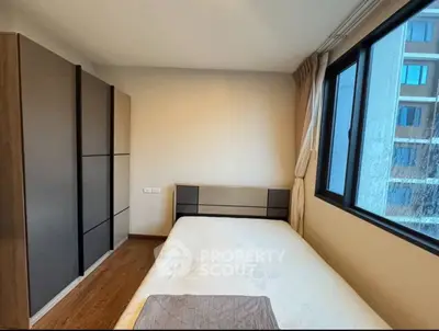 Cozy bedroom with large window and modern wardrobe in urban apartment.
