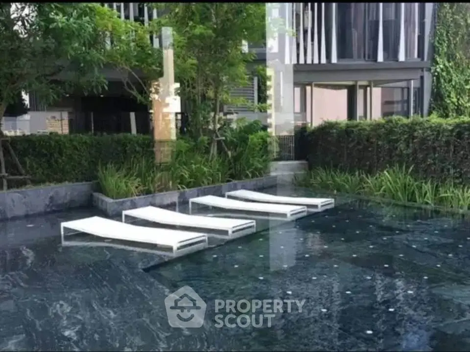 Luxurious modern pool area with sleek sun loungers and lush greenery in a contemporary residential complex.