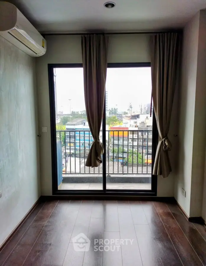 Modern apartment with large window and balcony view, featuring sleek wooden flooring and neutral curtains.
