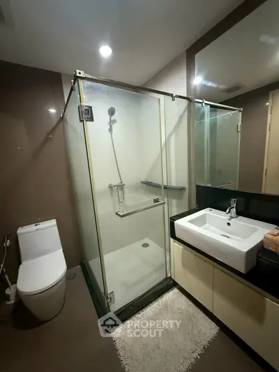 Modern bathroom with glass shower and sleek fixtures in contemporary apartment.