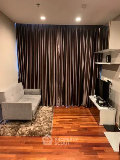 Modern living room with sleek design, featuring a cozy gray sofa, elegant curtains, and a flat-screen TV on wooden flooring.