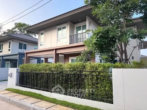 Modern two-story house with lush greenery and stylish fence in a serene neighborhood.