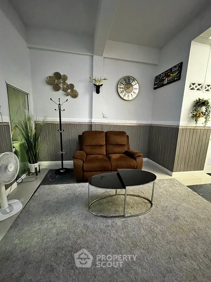 Cozy living room with modern decor, featuring a plush brown sofa, stylish wall clock, and elegant coffee table.