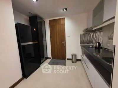 Modern kitchen with sleek appliances and wooden door, featuring a black fridge and stainless steel sink.