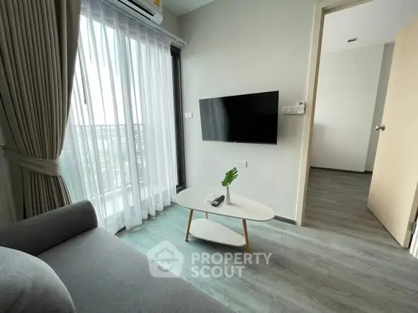 Modern living room with sleek design and natural light, featuring a wall-mounted TV and stylish furniture.