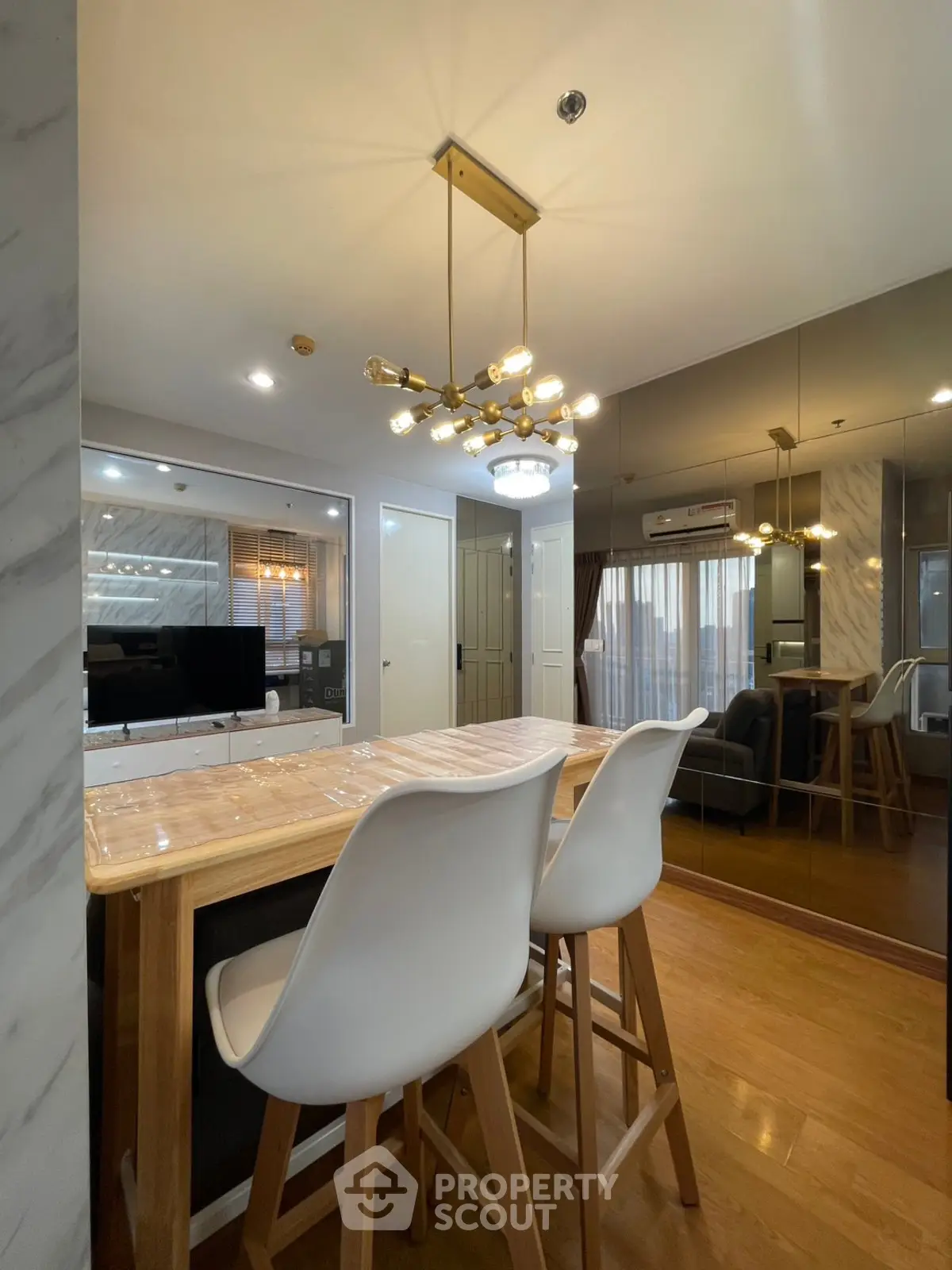 Modern living room with stylish chandelier and mirrored wall, featuring sleek wooden flooring and contemporary furniture.