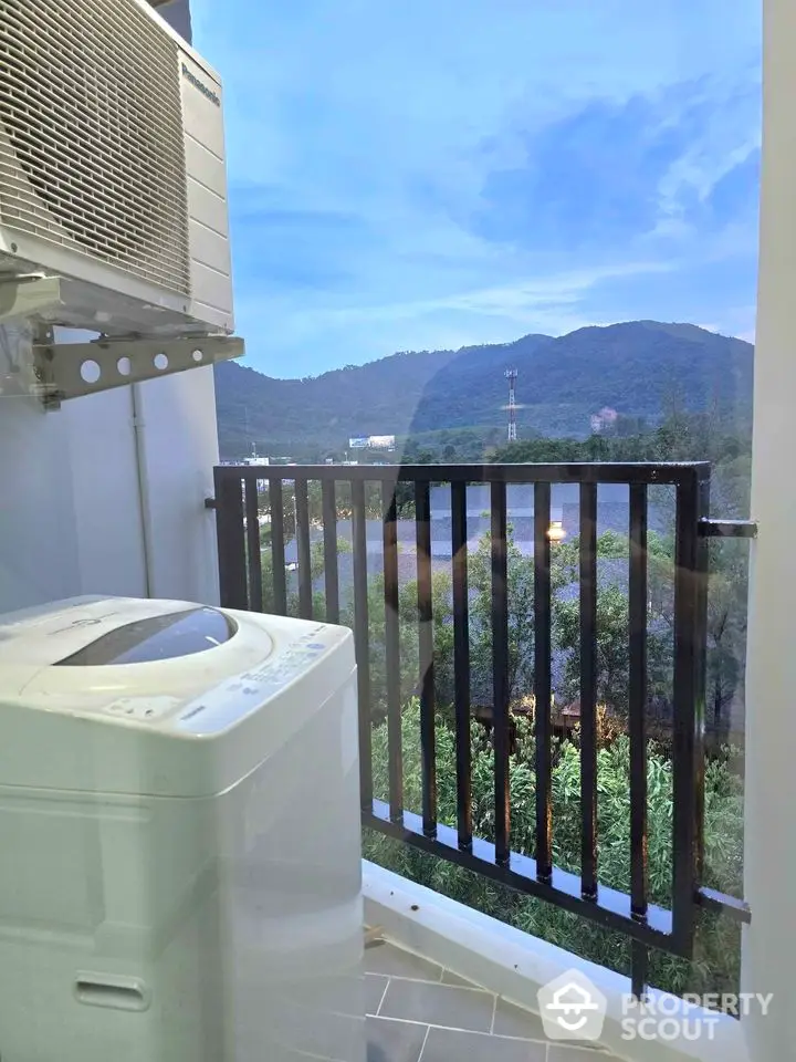 Scenic balcony view with washing machine overlooking lush green hills and clear blue sky.