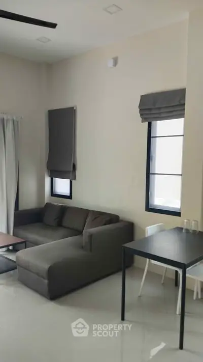 Modern living room with sleek gray sofa and dining table, featuring minimalist design and natural light.