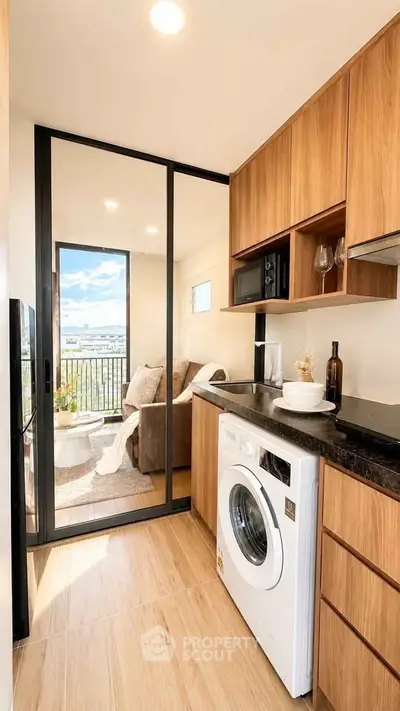 Modern kitchen with washing machine and open layout leading to cozy living room with balcony view.