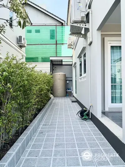 Modern exterior walkway with greenery and utility area in residential property